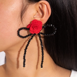 Détail de la boucle d'oreille rose en tissu rouge avec noeud perlé noir et glands