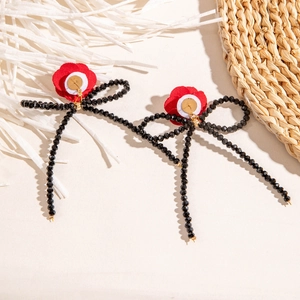 Vue détaillée de boucles d'oreilles fleurs rouges avec nœuds à pompons perlés noirs