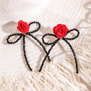 Détail de boucles d'oreilles nœuds avec roses rouges et pompons perlés noirs sur blanc