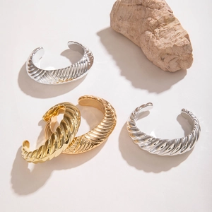 Détail de bracelets manchettes ouverts or et argent avec texture spirale et fini métallique