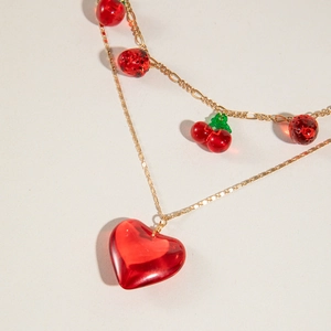 Close-up of double-layer gold necklace with red acrylic heart and fruit pendants