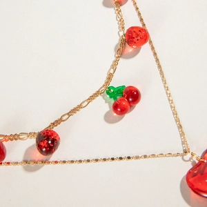 Close-up of double-layer gold necklace with red resin cherry and strawberry pendants
