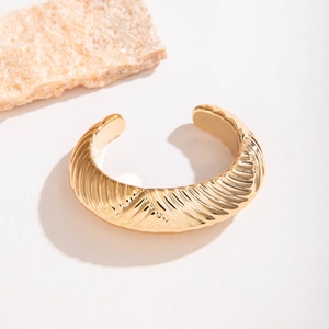 Vue détaillée d'un large bracelet doré avec une texture métallique rayée radiale