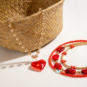 Detail of gold beaded necklace with red resin heart pendant and blue evil eye beads