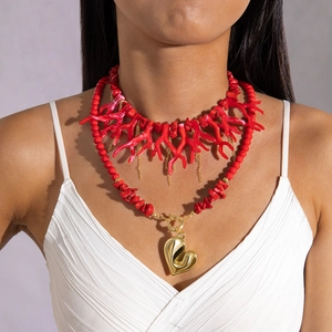 Detail of layered red coral-style beads and a large gold heart pendant on a white dress