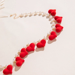 Close-up of velvet red heart pendants and white pearls on a layered necklace