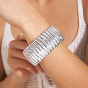 Gros plan sur un large bracelet manchette argenté avec un design texturé en vagues de plis