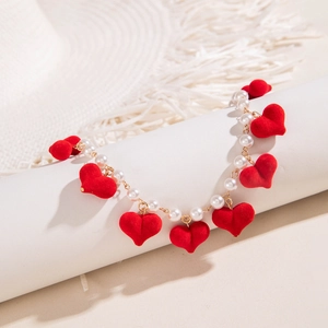 Macro detail of red velvet hearts and white pearls on a gold chain necklace