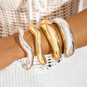 Gros plan de bracelets épais et ondulés en or et argent avec finition polie brillante