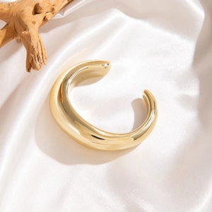 Gros plan d'un bracelet manchette doré épais minimaliste sur un tissu en soie blanche