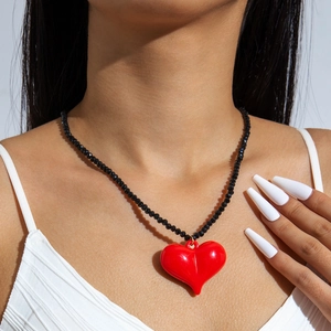 Close-up of a large glossy red heart pendant on a black beaded necklace for women