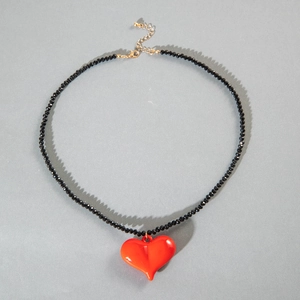 Flat lay of black beaded necklace featuring a glossy red acrylic heart pendant and gold clasp