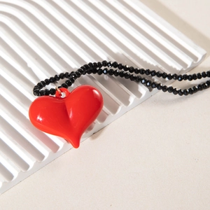 Detail of red acrylic heart pendant and black faceted beaded chain on a white display board