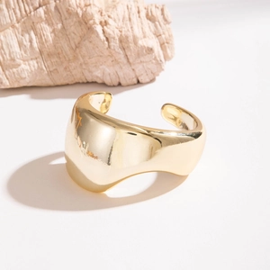Gros plan d'un bracelet manchette doré poli avec un design ondulé et asymétrique