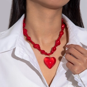 Detail of red acrylic heart pendant on irregular beaded necklace worn on white shirt