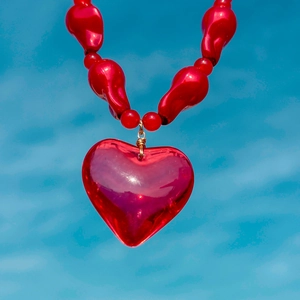 Close-up of a red acrylic heart pendant on a beaded necklace with gold wire details