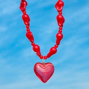 Close-up of red acrylic heart pendant and irregular beads against a bright blue sky background