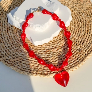 Detail of red acrylic heart pendant necklace with irregular beads on white stone plate