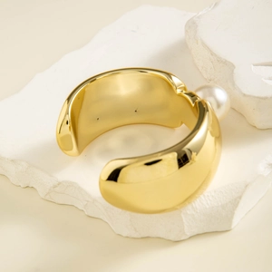 Détail d'un large bracelet jonc ouvert plaqué or avec une grande perle blanche