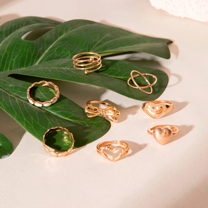 Rose gold stackable ring set with heart and bow designs on green leaf background
