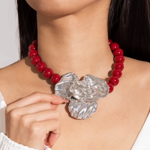 Macro view of vintage red acrylic beads with a large metallic silver flower pendant necklace