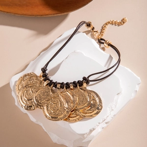 Detailed view of bohemian gold coin charms with hammered texture on brown braided cord