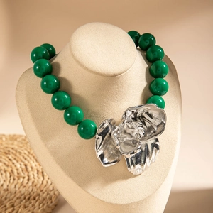 Detail of chunky green acrylic beads with a silver metallic flower pendant on a neck model