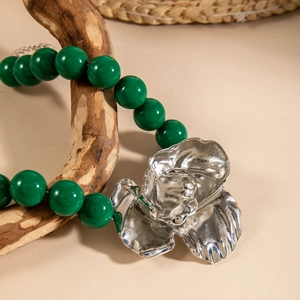 Close-up of green beaded necklace featuring a large irregular silver flower pendant