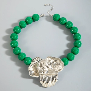 Macro view of green acrylic beads and a textured silver floral pendant on the necklace