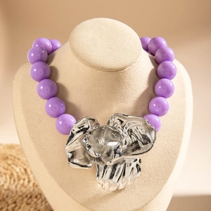 Detailed view of large silver metal flower pendant on a purple beaded necklace
