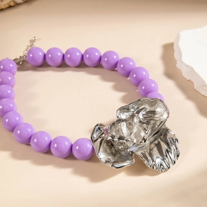 Macro detail of purple resin beads with a silver metallic floral pendant on beige surface