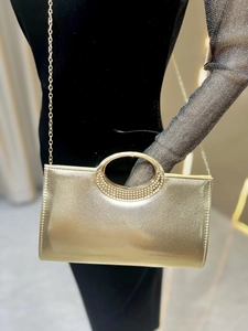 Detail of gold evening bag with rhinestone handle and metal chain on black dress