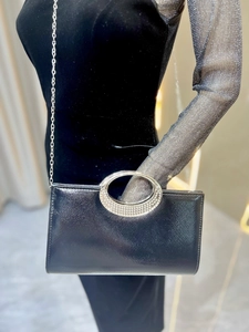 Detail of black evening clutch with rhinestone handle and silver chain on model