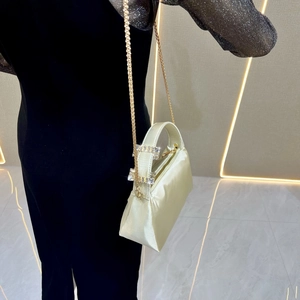 Detailed macro of ivory satin clutch bag featuring gold chain and rhinestone accents