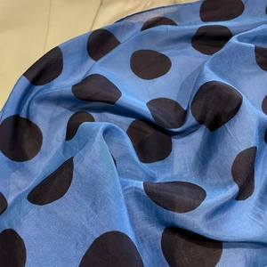 Dettaglio di un foulard in seta a pois blu con trama liscia e pieghe morbide ed eleganti