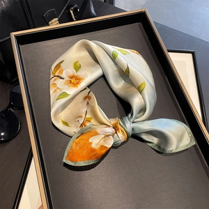 Elegant floral silk scarf in light green on a premium black leather tray with sunglasses