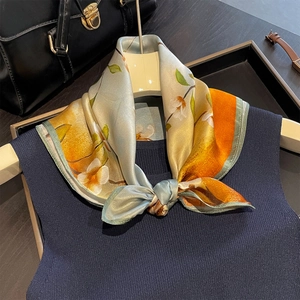 Silk scarf with citrus print and light blue base tied in a bow on a navy knit sweater