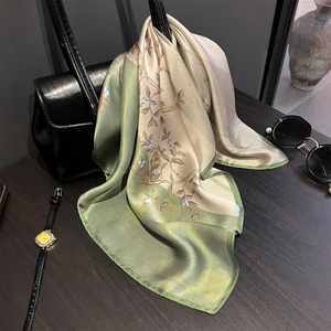Elegant silk floral scarf in green and champagne draped on a black handbag with accessories