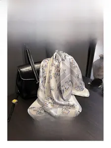 Silk neck scarf with blue butterfly print elegantly draped over a black leather handbag