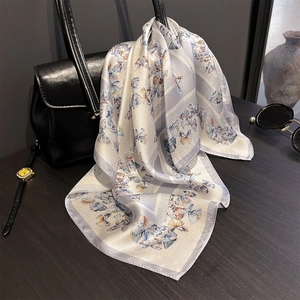 Silk scarf with butterfly print elegantly draped over a black leather handbag with accessories