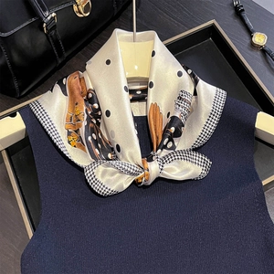 Dettaglio di un foulard in seta con pois e motivi equestri annodato a fiocco su un top