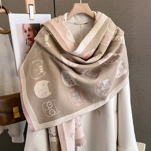 Détail d'une écharpe douce aspect cachemire avec motifs chats et franges sur un manteau
