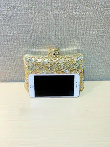 Close-up of golden evening clutch with floral rhinestone patterns and phone size comparison
