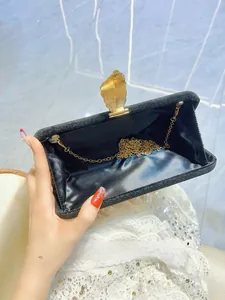 Detailed view of black velvet evening clutch with golden leaf clasp and light blue lining