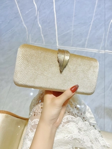 Detail of champagne gold evening clutch featuring a decorative metal leaf clasp