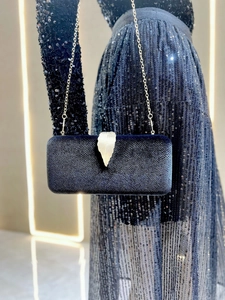 Detail of navy velvet evening clutch bag with ornate gold leaf clasp and metal chain strap