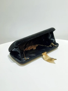 Detail view of black velvet clutch bag with golden leaf clasp and metal chain strap