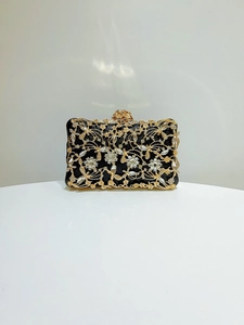 Detail of luxury evening clutch featuring golden floral hollow-out work and crystal accents