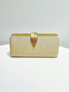 Detail of champagne gold evening clutch featuring a metal leaf clasp and pearly texture