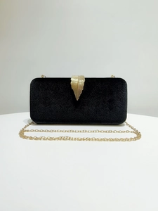Detail of black velvet evening clutch featuring an ornate gold leaf metal clasp and chain